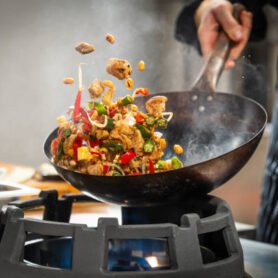 Unrecognizable male chef tossing vegetables and meat in the air while stir frying in a wok in a professional kitchen.